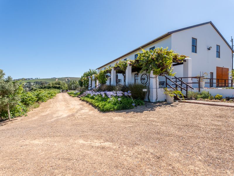 A charming farm-style building featuring a covered pergola, gravel driveway, and landscaped garden, set against a scenic rural landscape.