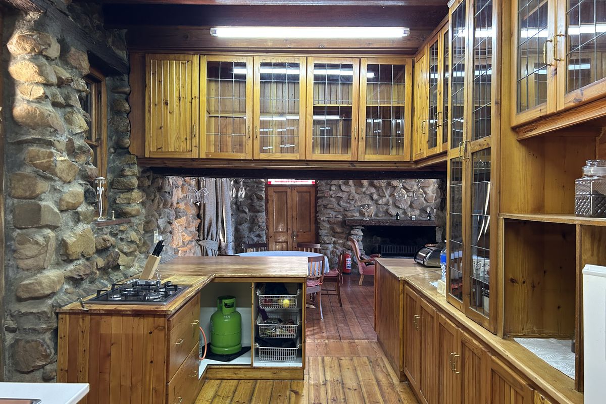 Rustic kitchen featuring extensive timber cabinetry, stone wall accents, exposed timber beams, and a built-in gas hob, opening into a cozy living area.