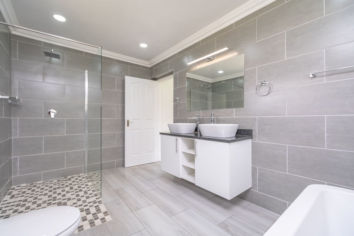 Modern bathroom featuring a double vanity with vessel sinks, a glass-enclosed walk-in shower, and contemporary grey wall tiling.