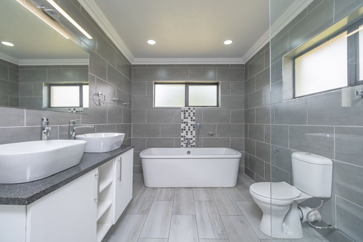 Modern bathroom featuring a freestanding bathtub, dual vessel sinks on a vanity, and a glass-enclosed shower area with contemporary grey tiling.