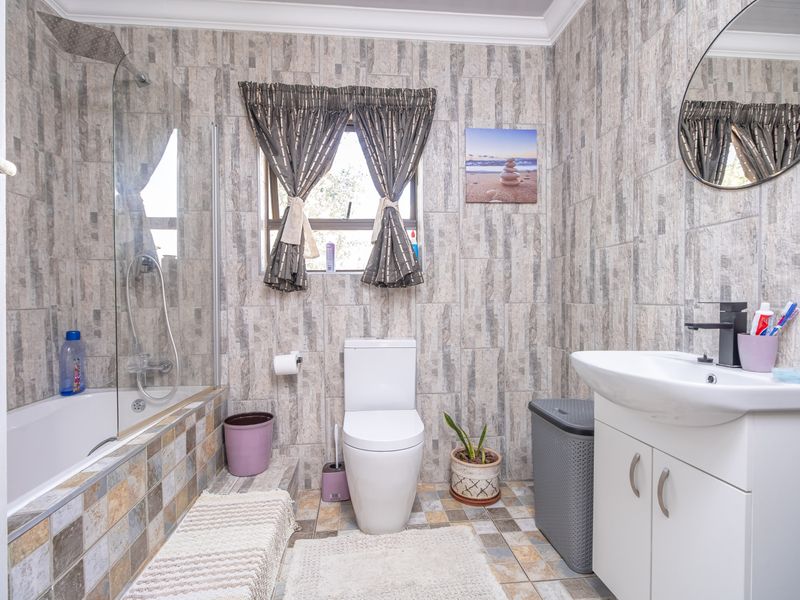 A functional bathroom featuring a glass-enclosed shower over the bathtub, a modern vanity basin, and a toilet, finished with textured wall tiling.