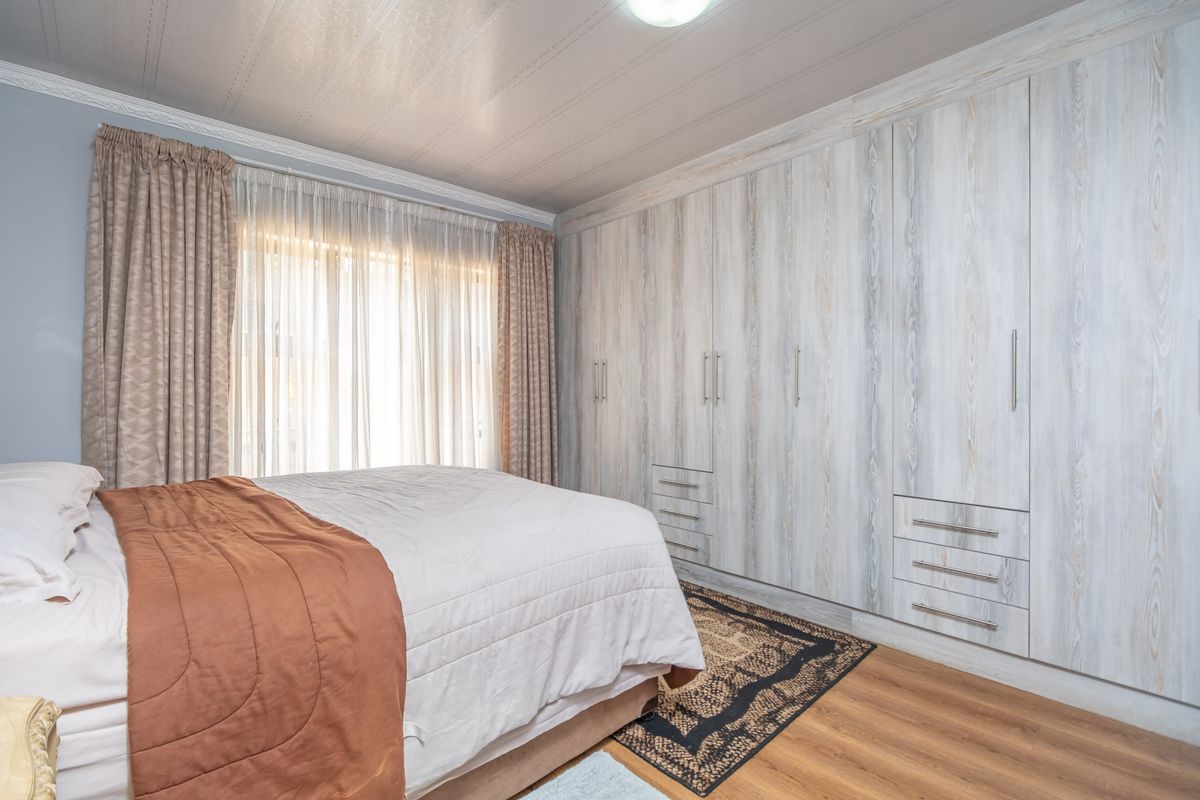 A well-maintained bedroom featuring extensive built-in cabinetry with a light wood finish, laminate flooring, and large windows with curtains.