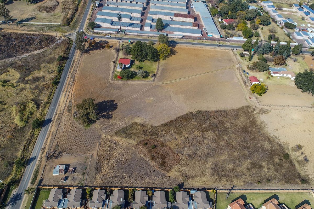 Aerial view of a large vacant residential plot featuring open land, perimeter fencing, and proximity to established residential and commercial areas.
