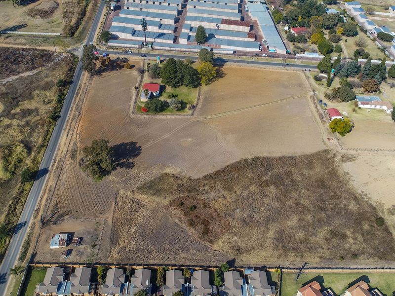 Aerial view of a large vacant residential plot featuring open land, perimeter fencing, and proximity to established residential and commercial areas.
