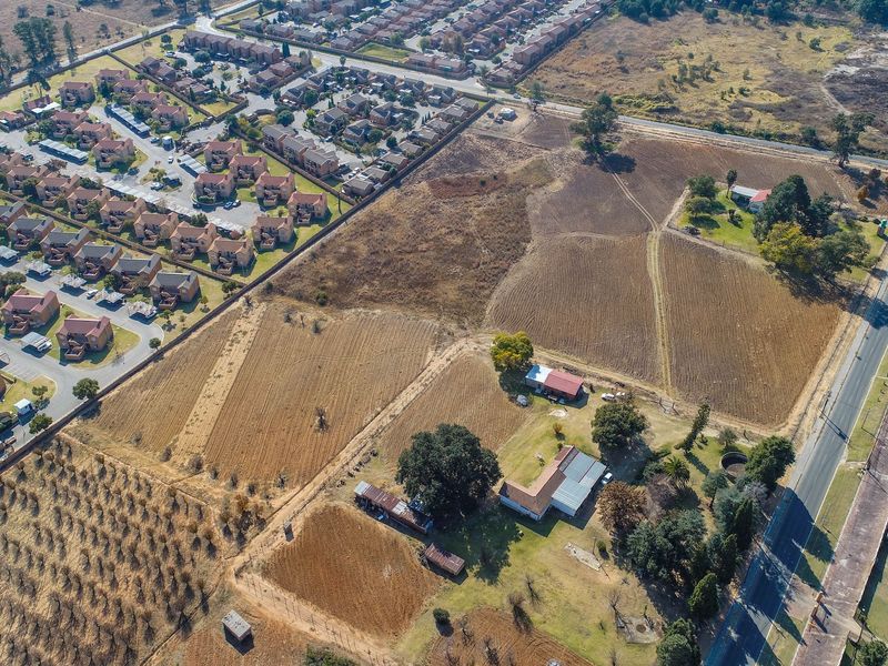 Aerial view of a large residential vacant land plot featuring existing outbuildings, mature trees, and perimeter fencing adjacent to a suburban development.