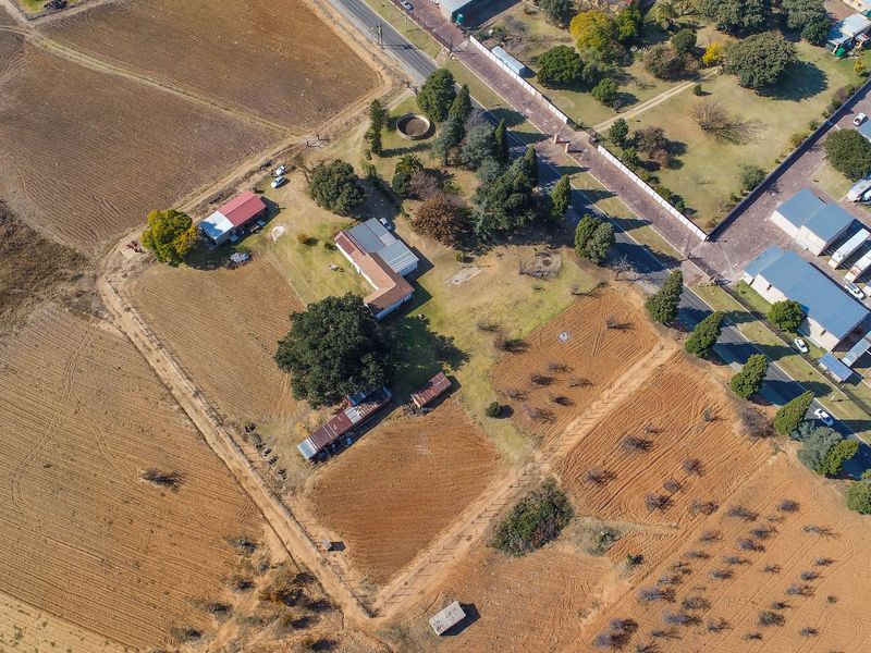 Aerial view of a residential vacant land property featuring a main dwelling, multiple outbuildings, established trees, and fenced boundaries.