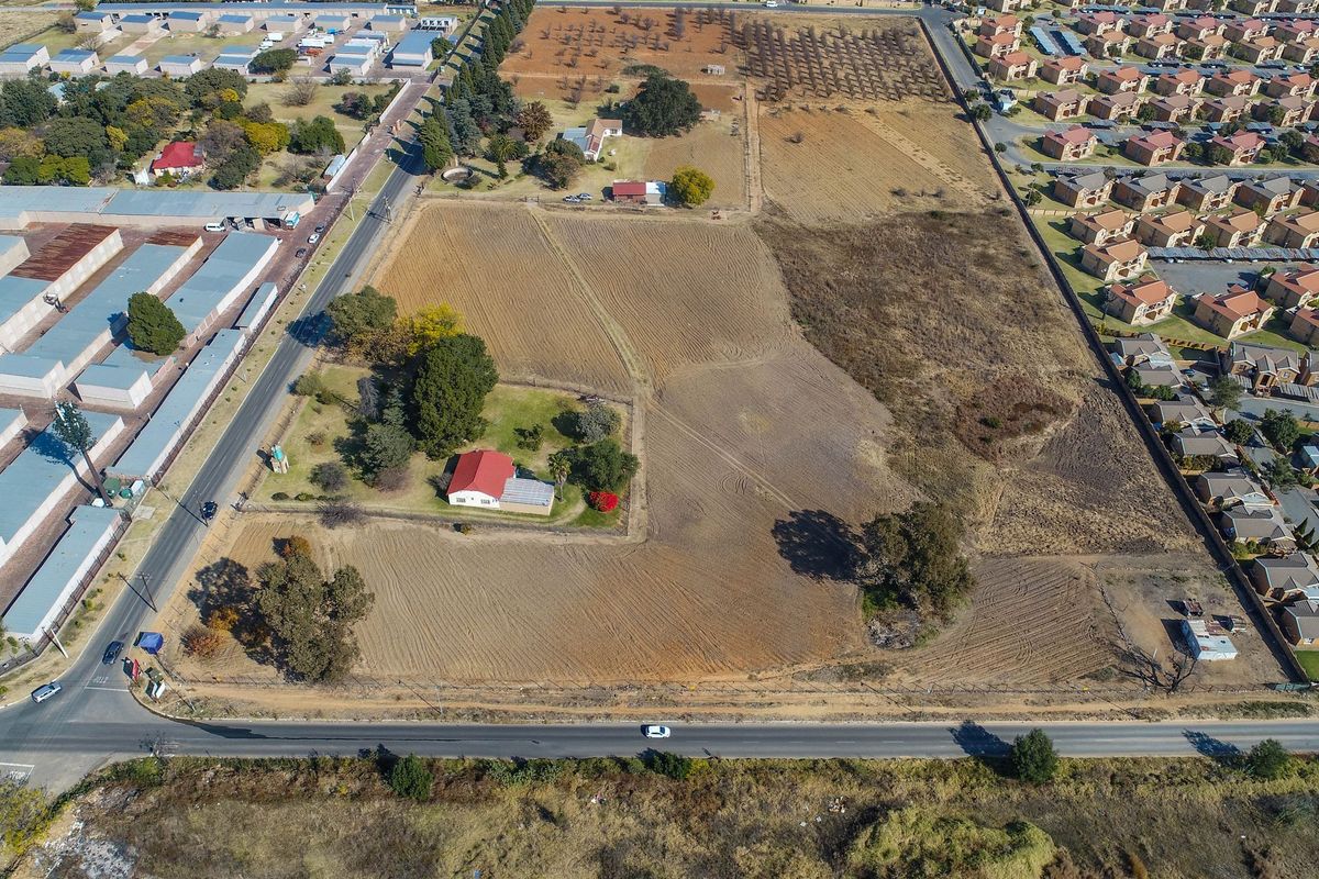 Aerial view of a large vacant residential land parcel featuring established trees, perimeter fencing, and an existing small dwelling on the property.
