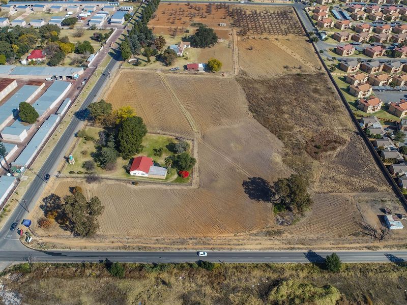 Aerial view of a large vacant residential land parcel featuring established trees, perimeter fencing, and an existing small dwelling on the property.