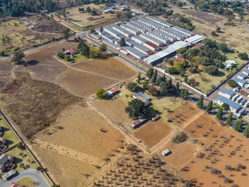 An aerial view of a large residential vacant land plot featuring established trees, perimeter fencing, and existing outbuildings in a semi-rural setting.
