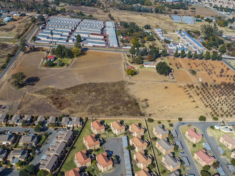 An aerial view of a large vacant residential land parcel situated adjacent to established housing developments and commercial storage facilities.