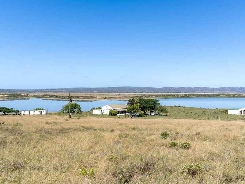 A wide-angle view of a rural farm property featuring a farmhouse and outbuildings situated near a large lake and open pasture land.