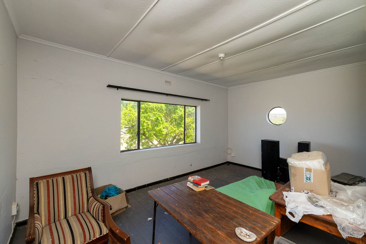 A living room space featuring a mix of rectangular and circular windows, timber flooring, and visible wear on the wall and ceiling finishes.