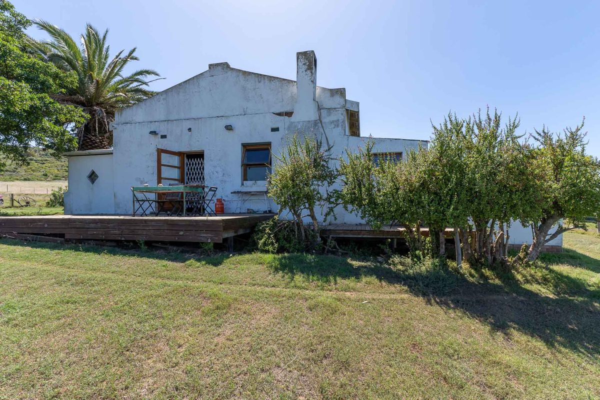 Rear view of a farm cottage featuring a timber deck, white rendered walls with visible weathering, and a prominent chimney.