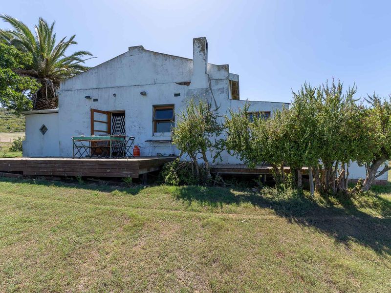 Rear view of a farm cottage featuring a timber deck, white rendered walls with visible weathering, and a prominent chimney.