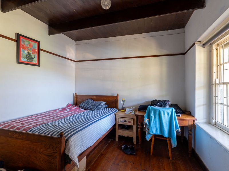 A bedroom featuring exposed timber ceiling beams, original timber flooring, and a classic leaded glass window.