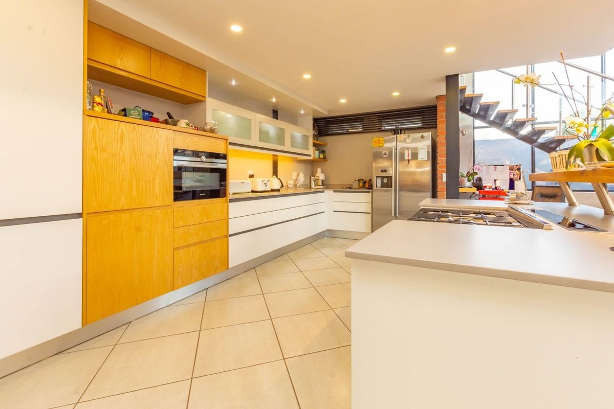 Modern kitchen featuring light wood cabinetry, white base units, stone countertops, integrated oven, and a central island with a built-in gas hob.