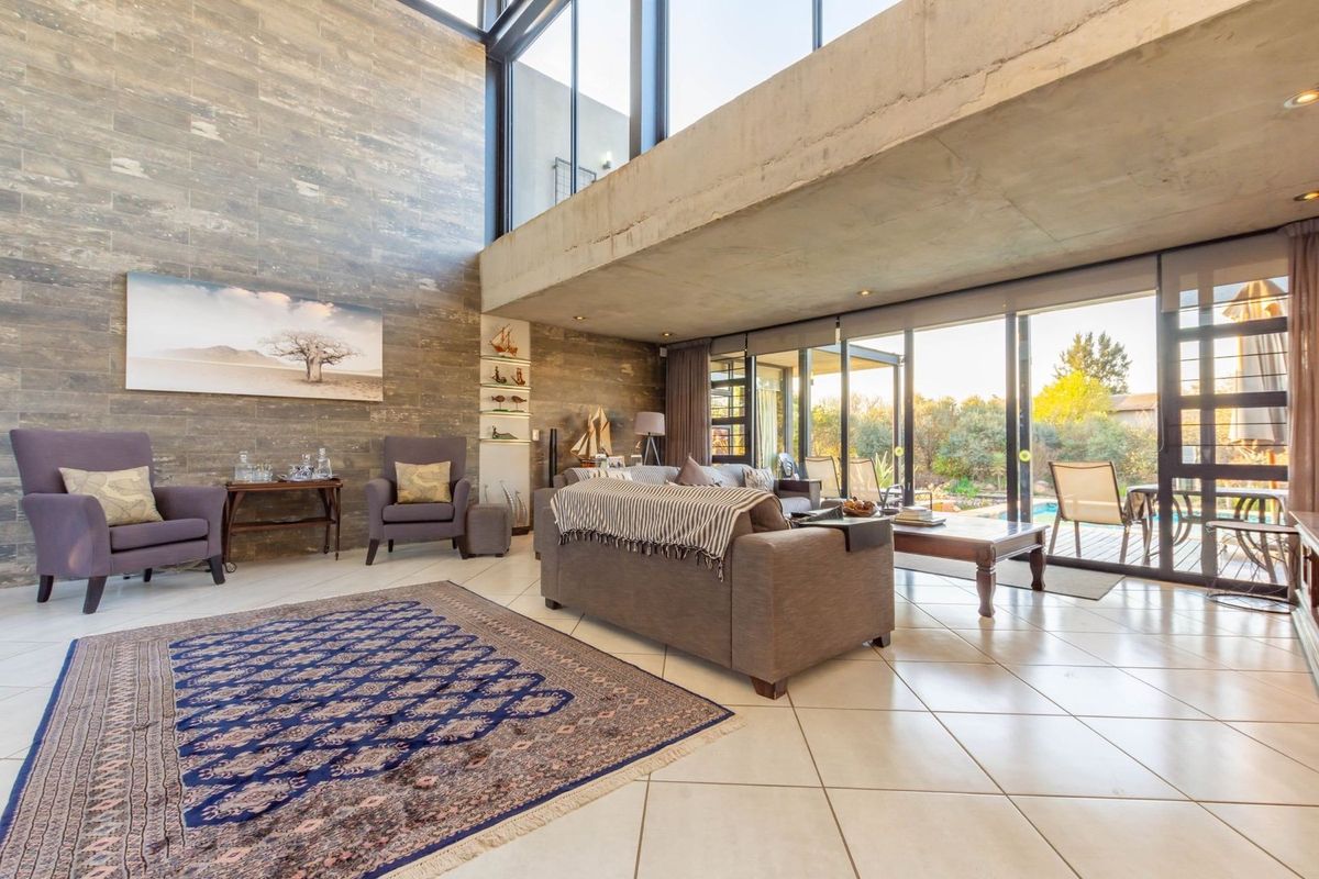 Spacious double-volume living area featuring floor-to-ceiling windows, exposed concrete architectural elements, and large format tiled flooring with seamless access to the outdoor patio.