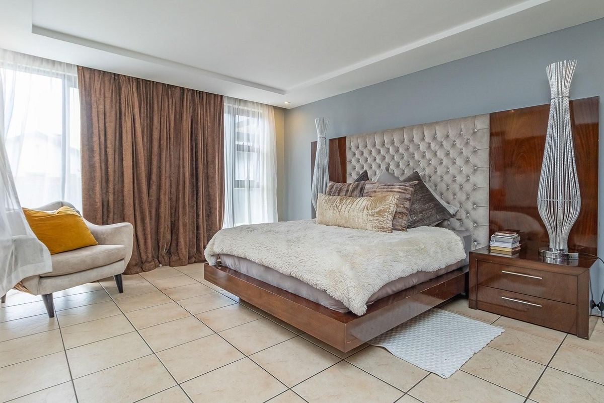 Spacious bedroom featuring tiled flooring, a built-in headboard with integrated side tables, and large windows with floor-to-ceiling curtains.