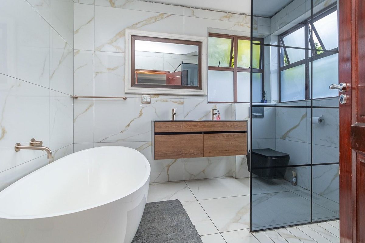 Modern bathroom featuring a freestanding bathtub, wall-mounted wooden vanity with dual basins, and a glass-enclosed shower area with marble-look wall tiles.