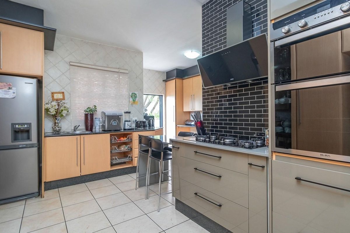 Modern kitchen featuring light wood cabinetry, dark subway tile backsplash, built-in oven, gas hob, extractor fan, and tiled flooring.