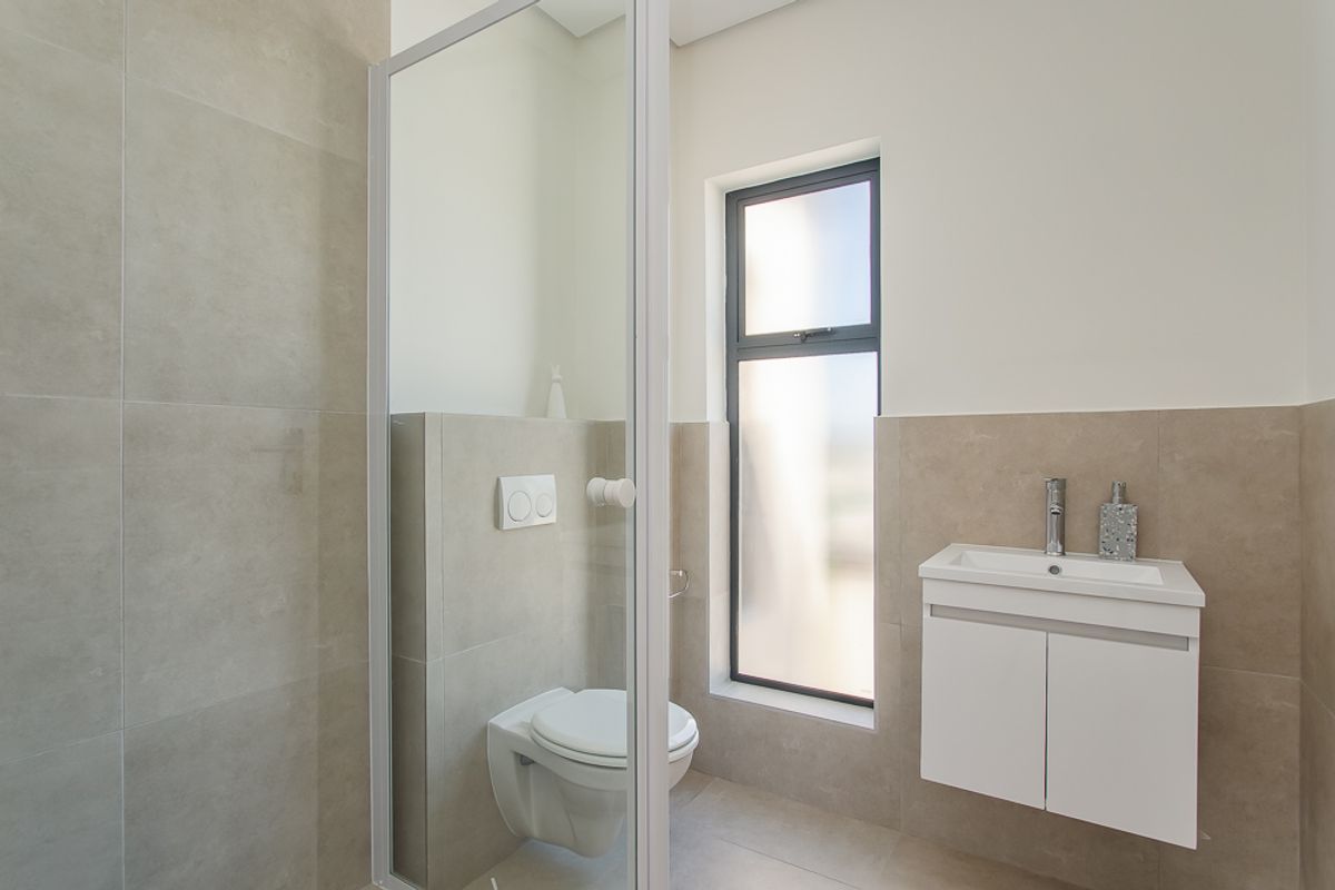 Modern bathroom featuring a wall-mounted toilet, a sleek vanity with basin, and a glass-enclosed shower with neutral floor-to-ceiling tiling.