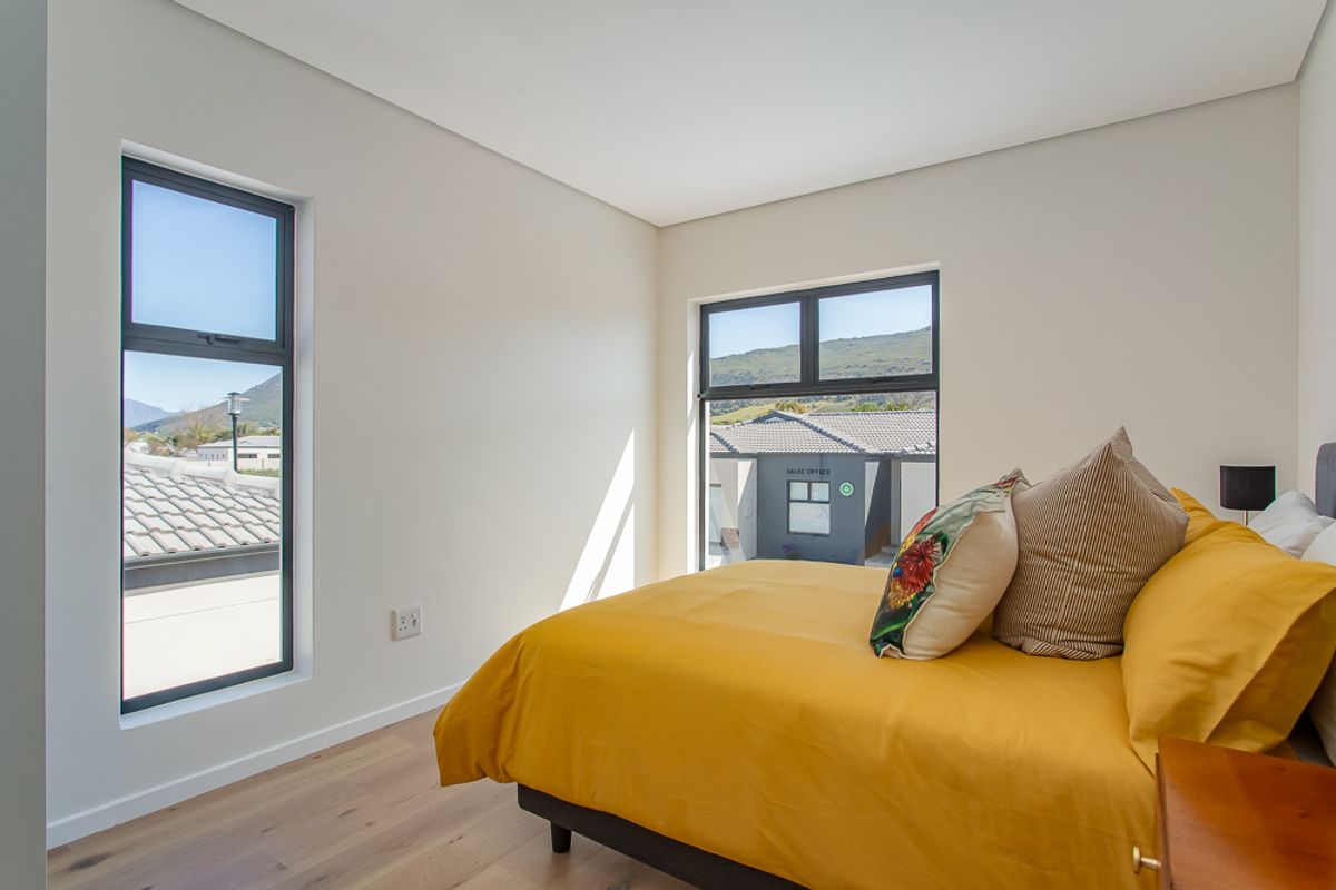 A bright and modern bedroom featuring light wood-look flooring, neutral walls, and large windows with views of the surrounding estate.