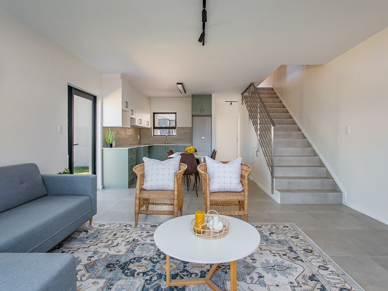 Open-plan living area featuring a modern kitchen with sage cabinetry, tiled flooring, and a staircase with a metal balustrade.