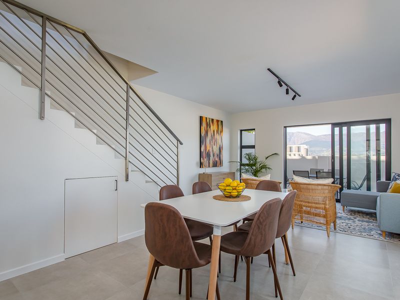 Open-plan living and dining area featuring modern tiled flooring, a sleek staircase with stainless steel balustrade, and sliding doors leading to a patio.