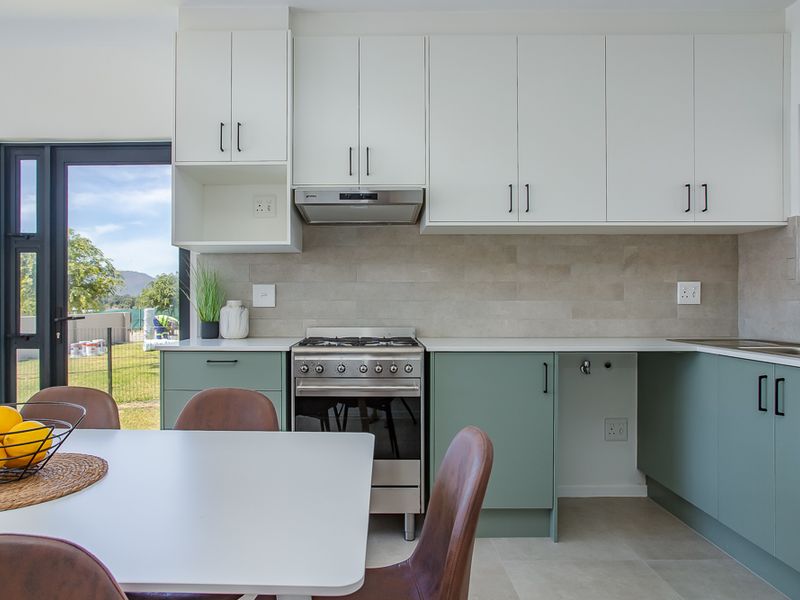 Modern open-plan kitchen featuring two-tone cabinetry, stone countertops, stainless steel gas stove, extractor fan, and direct access to the outdoor area.