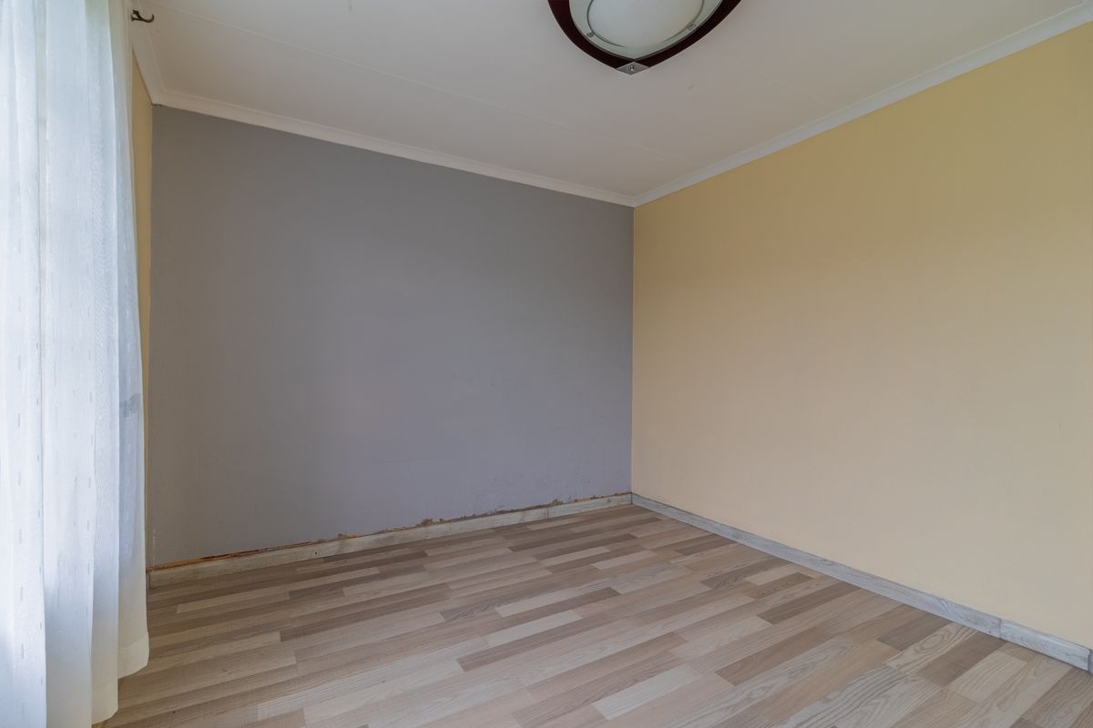 An empty bedroom featuring wood-look laminate flooring, dual-tone painted walls, and a central ceiling light fixture.