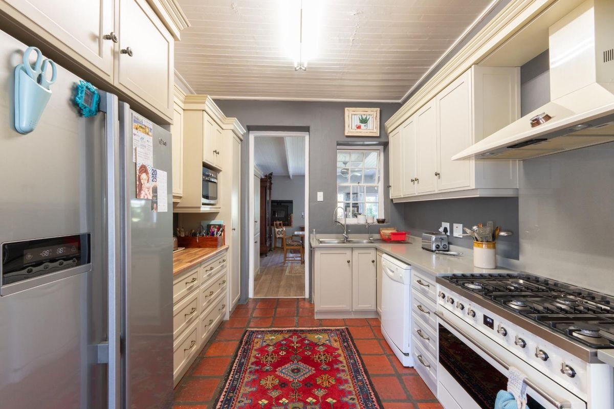 A functional galley-style kitchen featuring cream cabinetry, a gas hob, oven, extractor fan, and classic terracotta tile flooring.