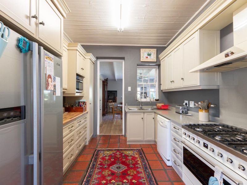 A functional galley-style kitchen featuring cream cabinetry, a gas hob, oven, extractor fan, and classic terracotta tile flooring.