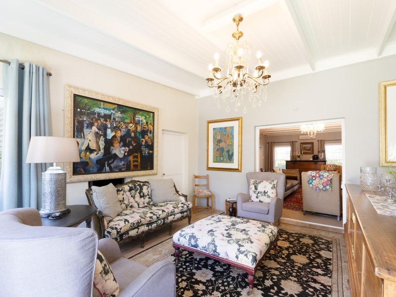 A bright and elegant living room featuring a classic chandelier, high tongue and groove ceilings, and a fireplace, with seamless flow into an adjacent room.