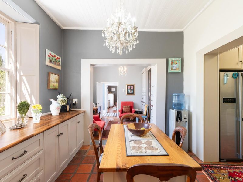 An open-plan dining area featuring terracotta flooring, custom built-in cabinetry with timber countertops, and a classic crystal chandelier under a beadboard ceiling.
