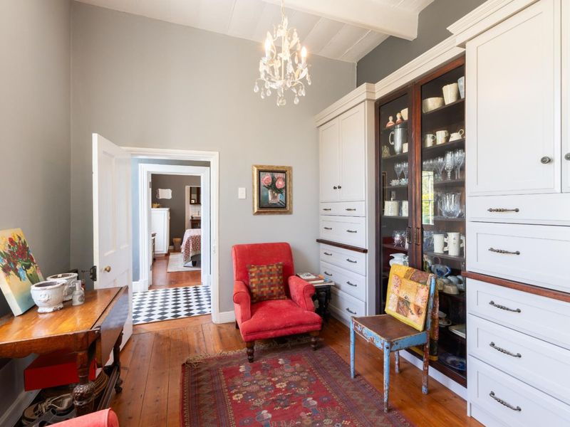 A cozy living space featuring classic timber flooring, high ceilings with exposed beams, and extensive built-in cabinetry with glass-fronted display shelving.