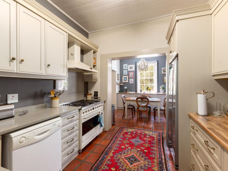 A well-appointed kitchen featuring classic shaker-style cabinetry, stone countertops, a gas range cooker, and traditional terracotta tile flooring, leading into an adjacent dining area.