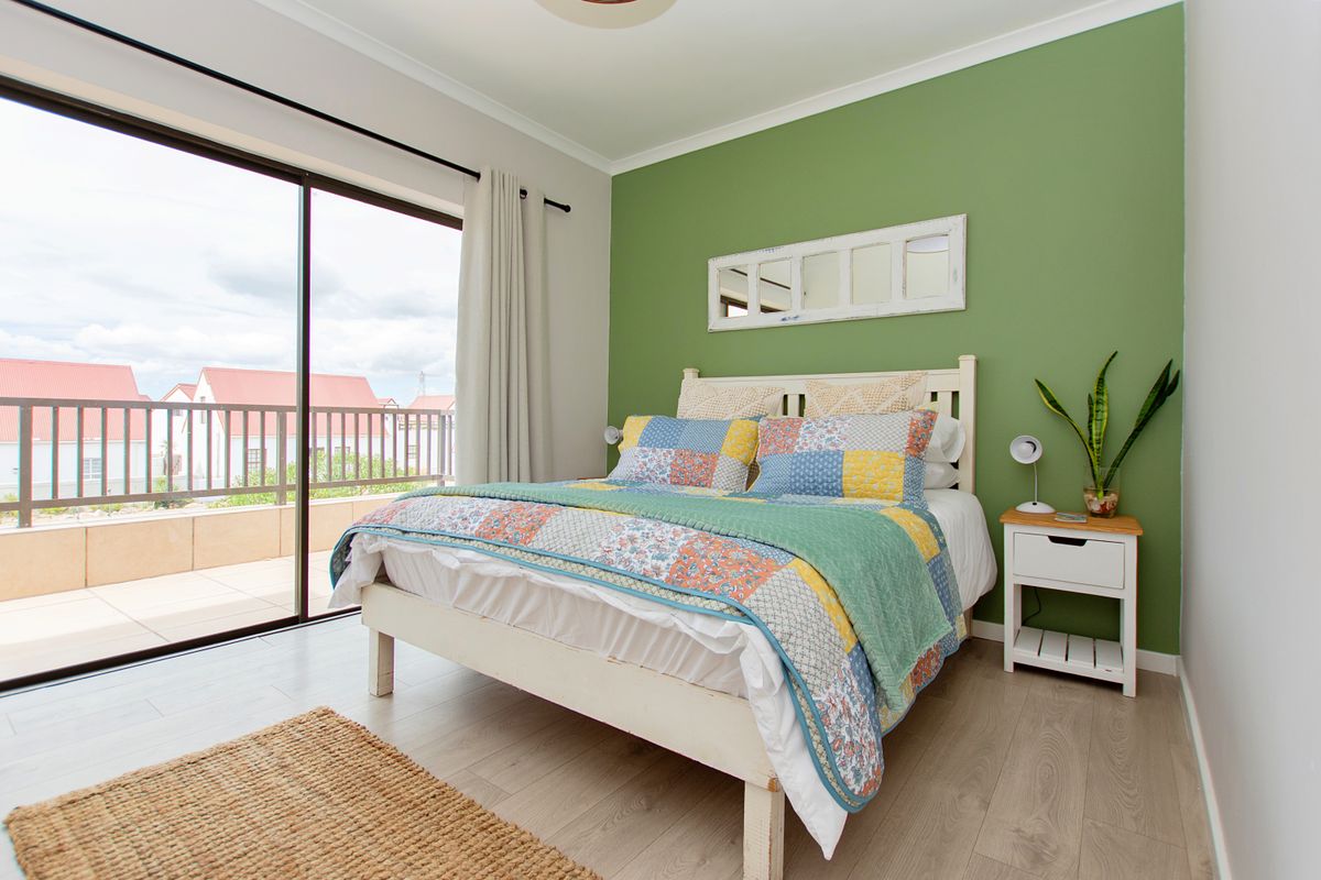 A bright bedroom featuring light wood-look flooring, a green accent wall, and large sliding glass doors providing access to a private balcony.