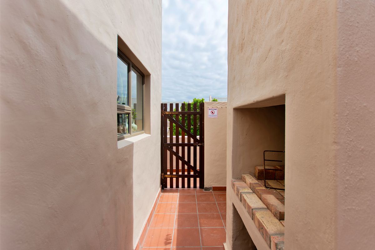 A narrow outdoor passage featuring a built-in brick braai area, tiled flooring, and a wooden gate leading to the exterior.