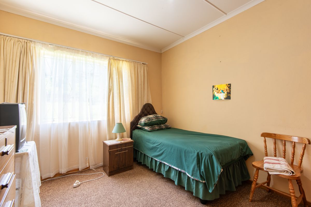 A simple bedroom featuring carpeted flooring, a large window with curtains, and neutral wall finishes.