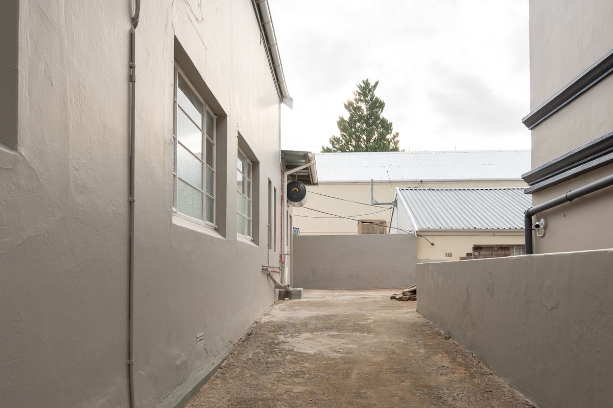 A narrow exterior side passage or courtyard area featuring painted masonry walls, concrete flooring, and exposed utility infrastructure.