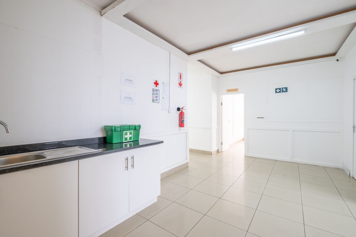 A functional office kitchenette area featuring a built-in sink, granite countertop, and tiled flooring, leading into a hallway.