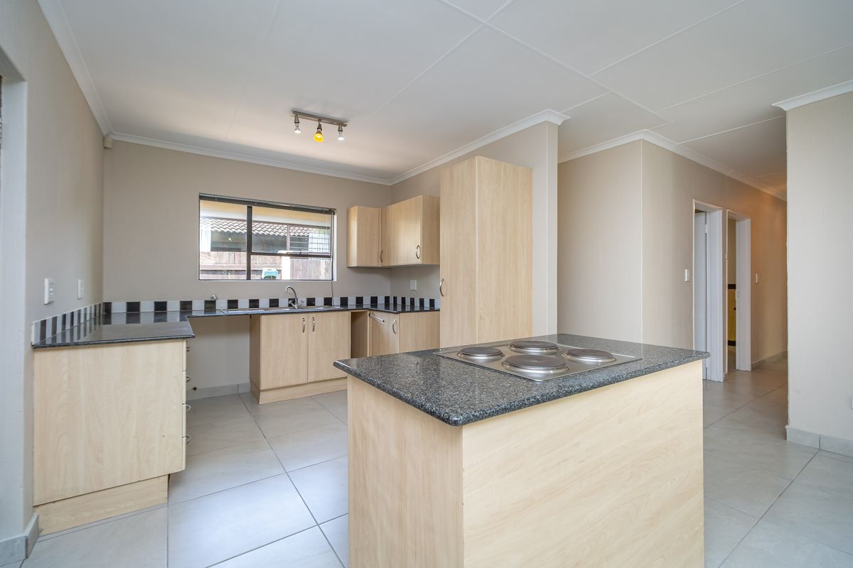 A functional kitchen featuring light wood cabinetry, granite countertops, a central island with a built-in electric hob, and tiled flooring.
