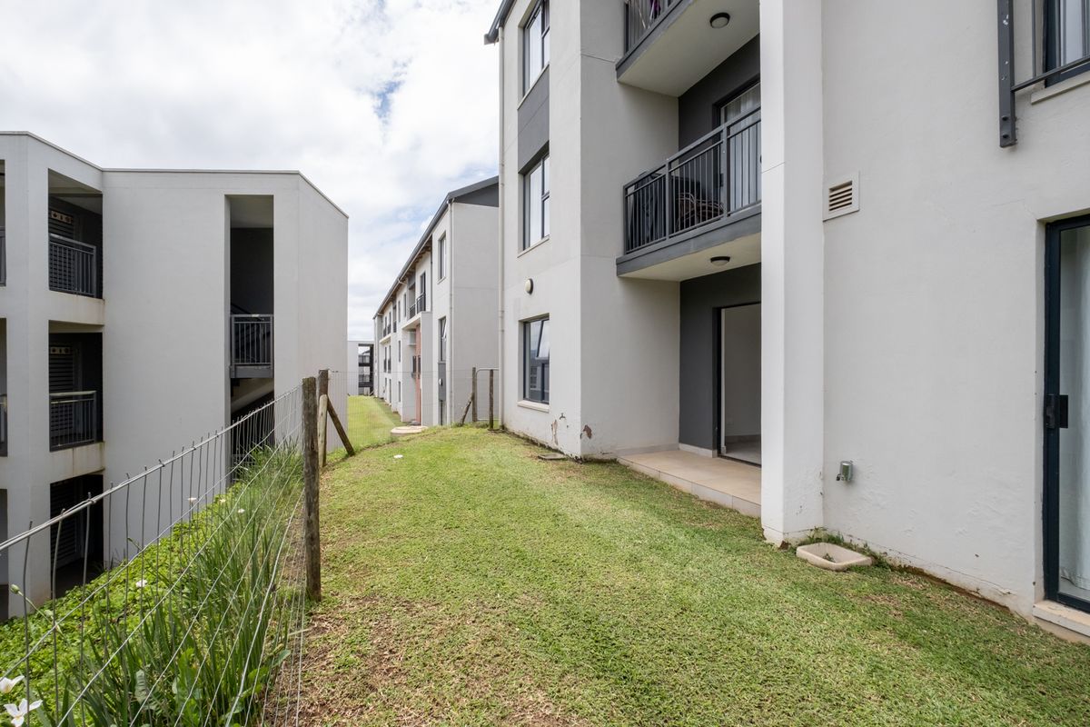 Exterior view of a modern apartment complex featuring ground floor patio access, private garden space, and upper-level balconies with metal railings.
