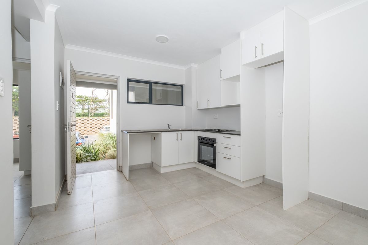 A clean, modern kitchen featuring white cabinetry, a built-in oven and hob, and tiled flooring, with direct access to an outdoor area.