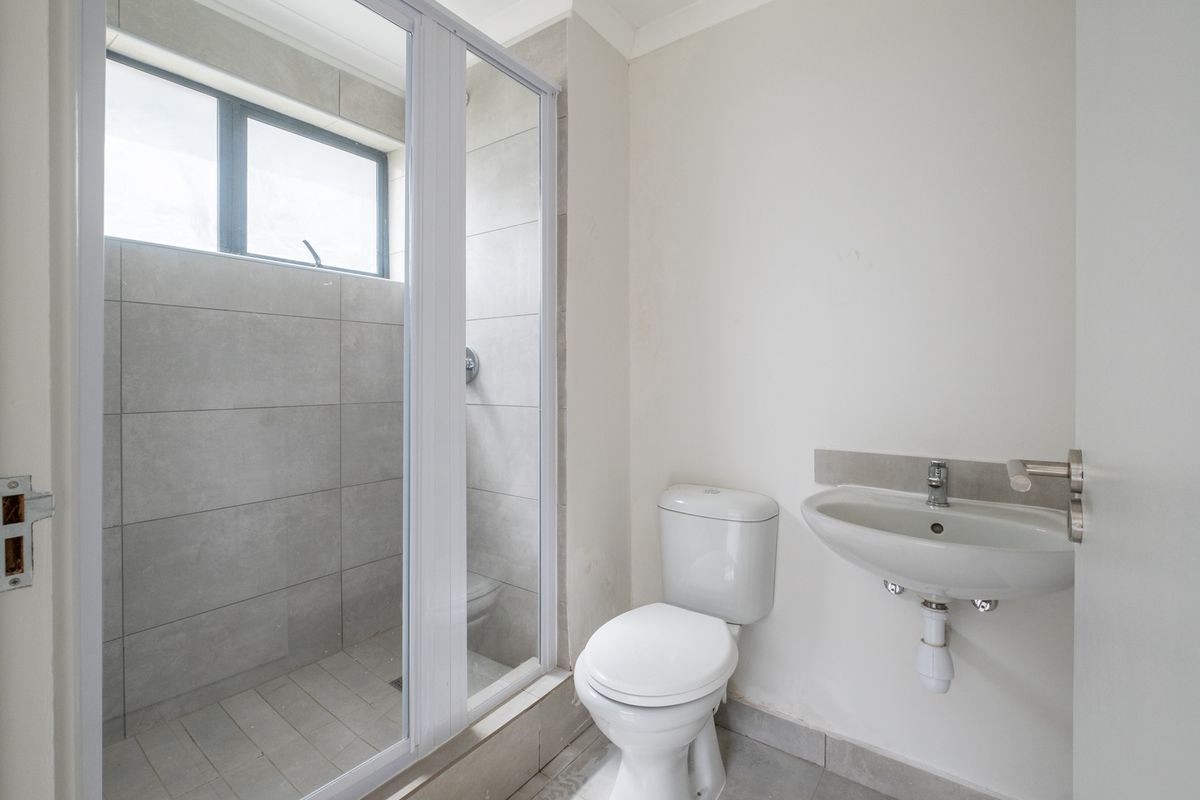 A functional bathroom featuring a walk-in shower with grey tiling, a standard white toilet, and a wall-mounted basin.