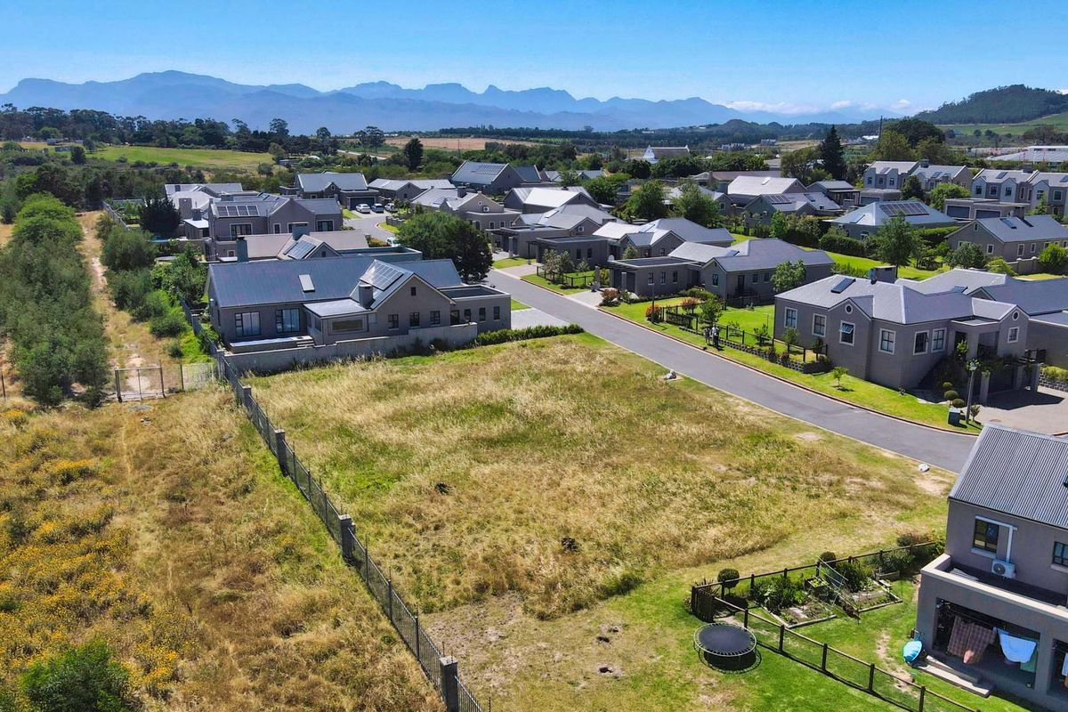 An aerial view of a vacant residential plot situated within a developed estate, featuring surrounding homes and mountain views.