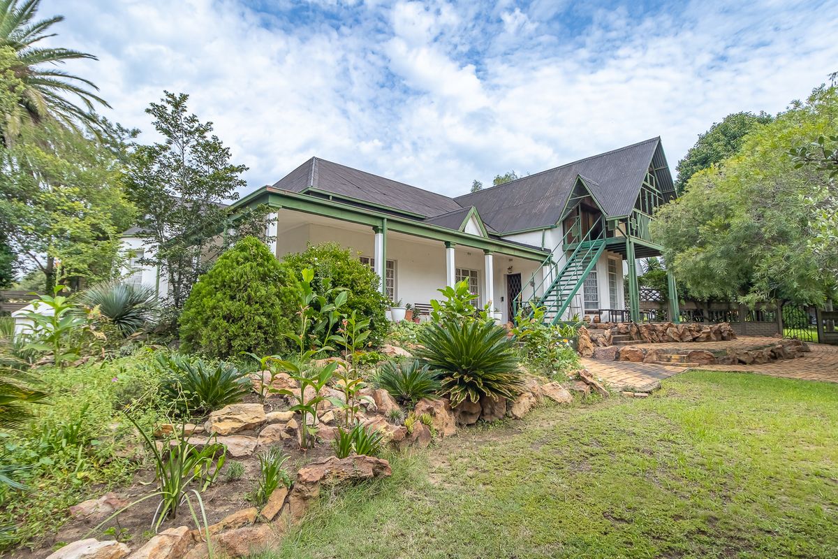 A charming character home featuring a wrap-around veranda, pitched roof, and an external metal staircase set within a lush, landscaped garden.
