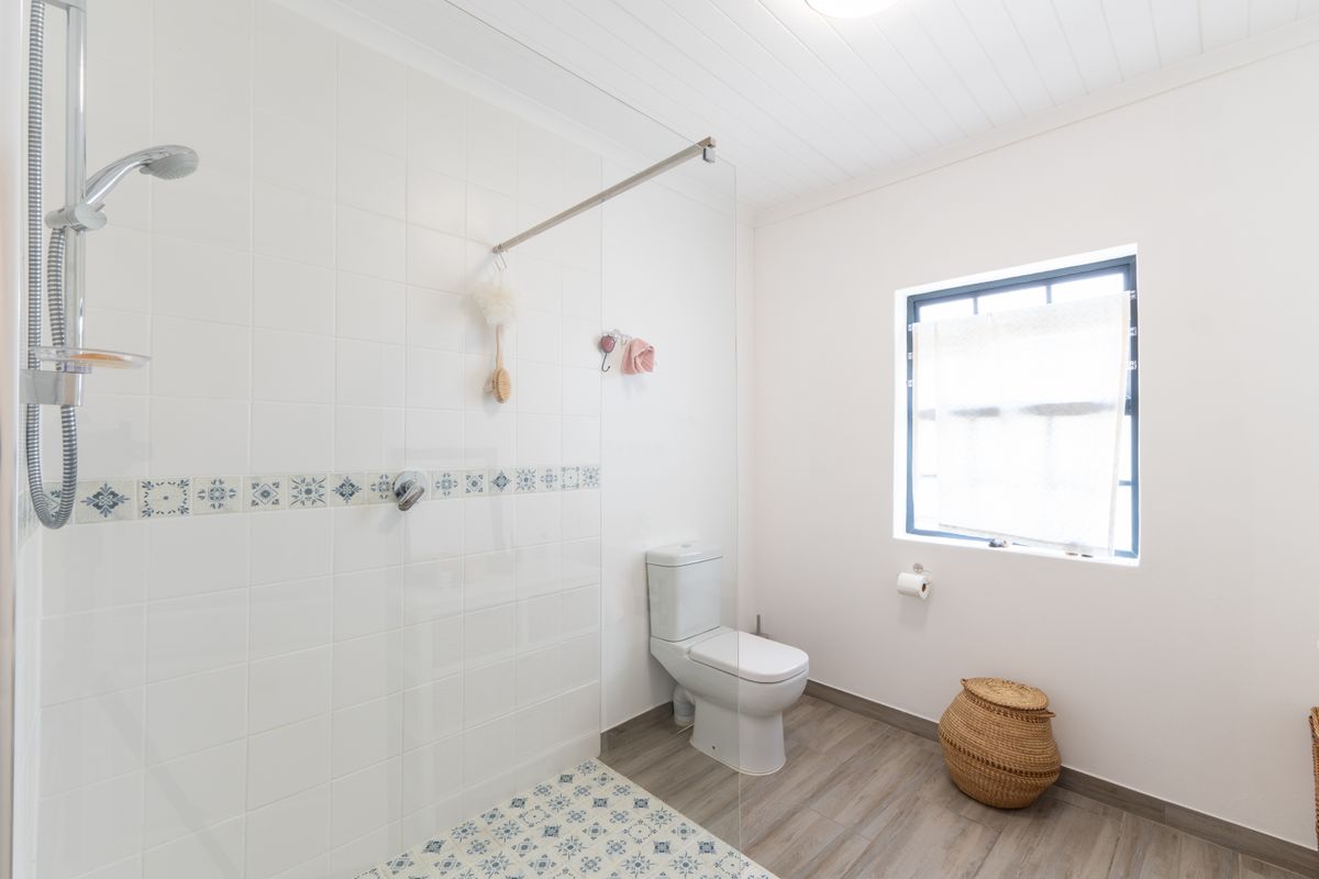 A clean, modern bathroom featuring a walk-in shower with glass screen, patterned tile accents, and a white toilet.