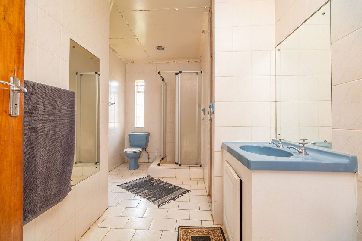 A dated bathroom featuring a blue vanity basin, a separate shower enclosure, and a toilet, finished with full-height wall tiling.