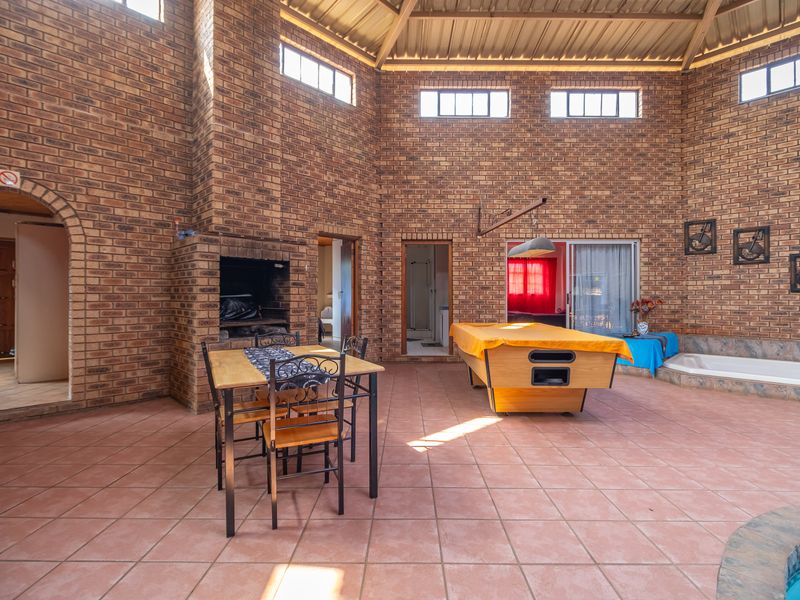 Spacious indoor entertainment area featuring exposed brick walls, a built-in fireplace, tiled flooring, and direct access to a swimming pool.